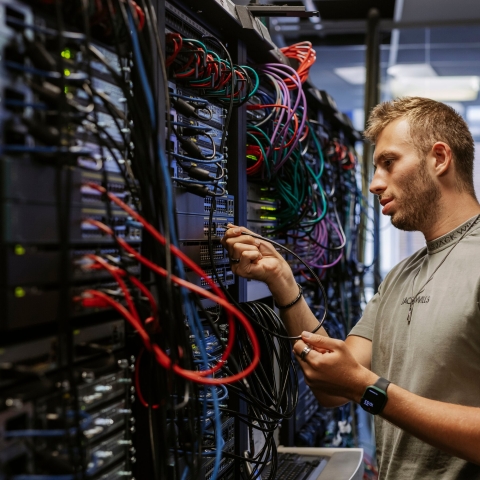 Student adjusts ethernet connections at a server board in Technology Facilities