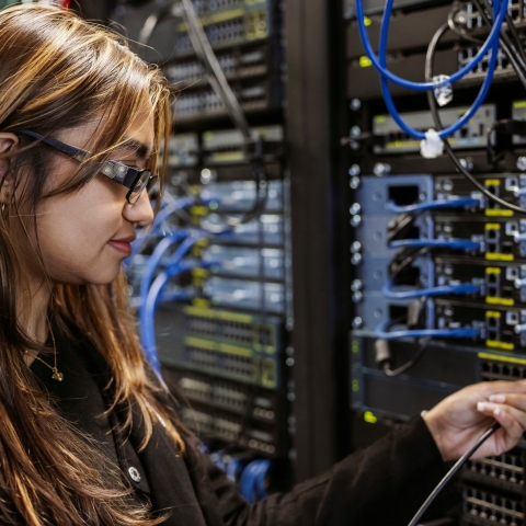 Student adjusts ethernet cables on server wall in Technology Facilities