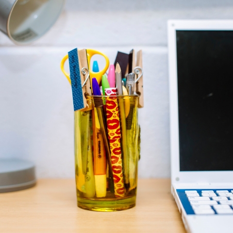 Close up of a laptop and a tumbler filled with stationery
