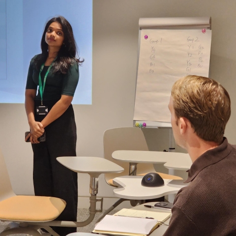 Girl standing in the distance in front of projector looking at man sitting down