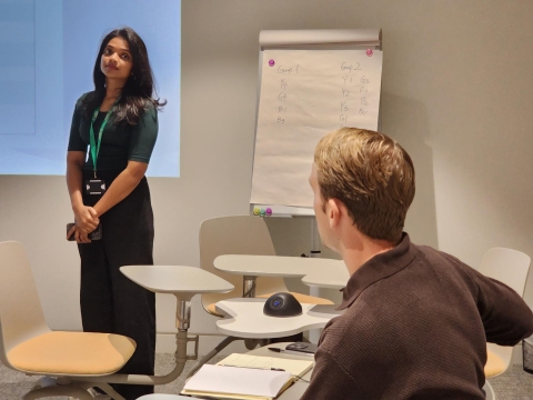 Girl standing in the distance in front of projector looking at man sitting down