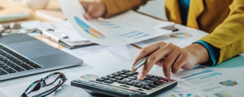 hands holding sheet with graph and typing on calculator